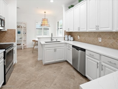 Kitchen featuring backsplash, appliances with stainless steel finishes, white cabinets, decorative light fixtures, and a peninsula