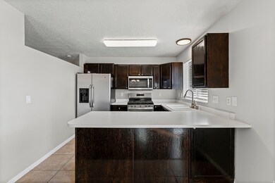 Kitchen with dark brown cabinets, light countertops, appliances with stainless steel finishes, a peninsula, and a textured ceiling