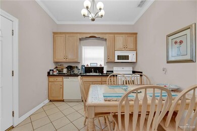 Kitchen featuring white appliances, decorative light fixtures, ornamental molding, light brown cabinetry, and a notable chandelier