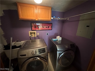 Laundry area with electric panel, a textured ceiling, cabinet space, and washing machine and dryer