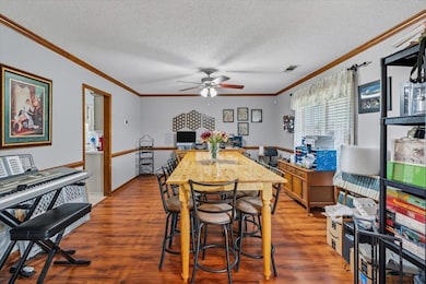 Dining area with wood finished floors, a textured ceiling, crown molding, and ceiling fan
