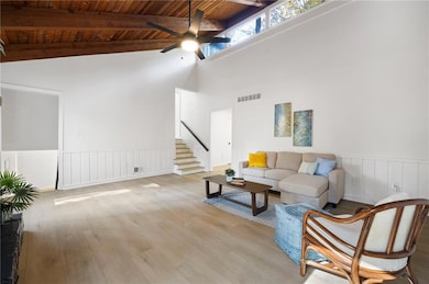 Living area with wood finished floors, a wood ceiling with exposed beams, wainscoting, high vaulted ceiling, and a ceiling fan
