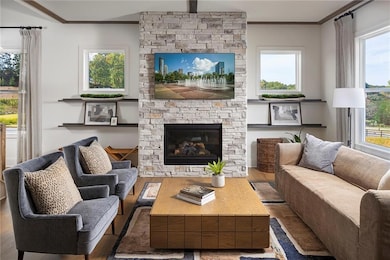 Living area featuring wood finished floors, a stone fireplace, with an abundance of light. Photo is representative of the Acworth Model Home. Designer features will vary.
