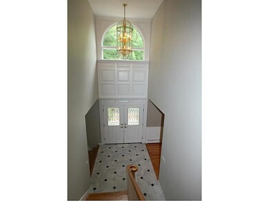Entry. View from the staircase toward the front door, grand 2 story foyer with marble tile and diamond shaped granite inlay, custom millwork, double entry doors, chandelier and expansive window for lots of natural light.