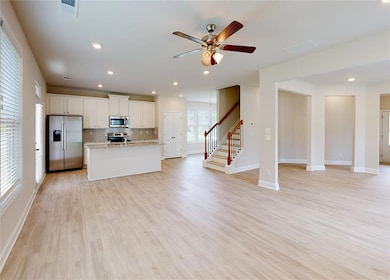 Kitchen featuring light stone countertops, white cabinets, appliances with stainless steel finishes, light hardwood / wood-style flooring, and a center island with sink