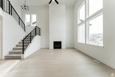 Unfurnished living room featuring a fireplace, stairway, a high ceiling, light wood-type flooring, and a ceiling fan