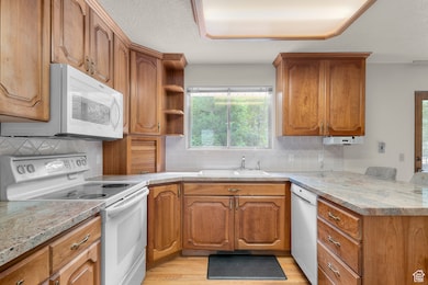 Kitchen with white appliances, brown cabinets, decorative backsplash, and a textured ceiling