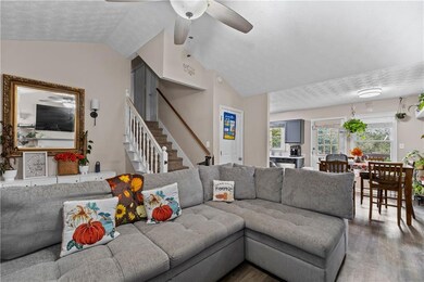 Living area with vaulted ceiling, wood finished floors, a textured ceiling, stairway, and ceiling fan
