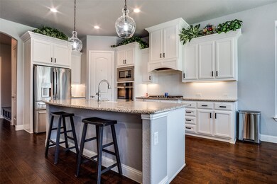 Kitchen featuring tasteful backsplash, white cabinetry, light stone counters, a breakfast bar area, and hanging light fixtures