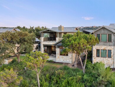 Rear view of property featuring stone siding, a balcony, a patio, and a chimney