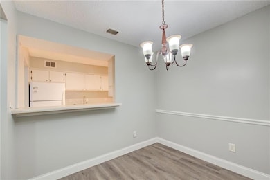 Unfurnished dining area featuring visible vents, baseboards, a textured ceiling, and wood finished floors