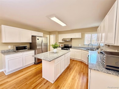 Kitchen with white cabinets, appliances with stainless steel finishes, light wood finished floors, a kitchen island, and light stone countertops