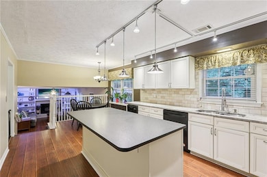 Kitchen with black dishwasher, backsplash, a center island, white cabinets, and a textured ceiling