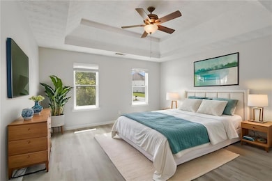 Bedroom featuring a raised ceiling, wood finished floors, baseboards, and a ceiling fan