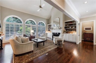 Living area with built in features, ceiling fan, dark wood-style floors, a fireplace, and ornamental molding