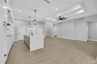 Kitchen with ceiling fan with notable chandelier, an island with sink, light hardwood / wood-style floors, and sink
