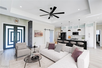 Living room featuring a barn door, light wood-style floors, ornamental molding, a tray ceiling, and a ceiling fan. Virtual Staging