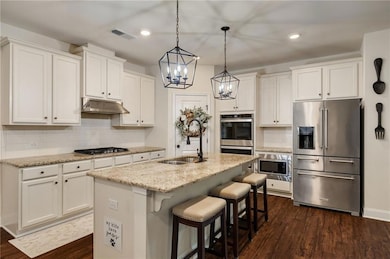 Kitchen with stainless steel appliances, a sink, under cabinet range hood, white cabinets, and recessed lighting