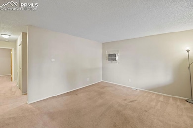 Empty room featuring light colored carpet, a textured ceiling, and an AC wall unit