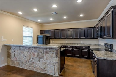 Kitchen with light stone counters, recessed lighting, visible vents, ornamental molding, and black appliances