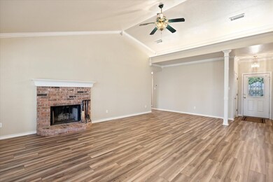 Living room with a fireplace, vaulted ceiling, crown molding, and laminate flooring