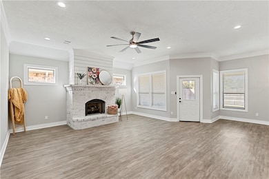Unfurnished living room with light wood finished floors, a brick fireplace, ceiling fan, ornamental molding, and recessed lighting