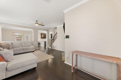 Living area featuring arched walkways, crown molding, stairway, dark wood finished floors, and ceiling fan