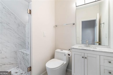 Main floor bathroom featuring toilet, a tiled  shower, vanity, and baseboards