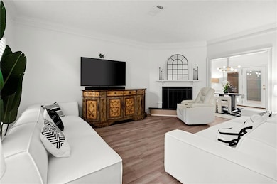 Living room with a fireplace with raised hearth, ornamental molding, wood finished floors, and a chandelier
