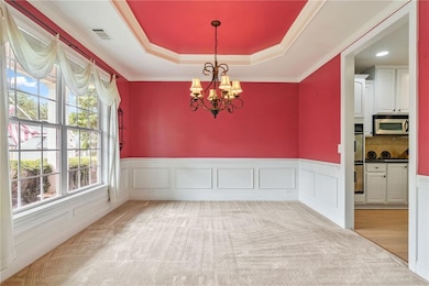 Formal dining area with a chandelier, a tray ceiling, wainscoting, crown molding, and light carpet