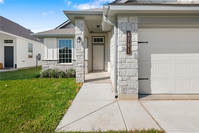 View of exterior entry featuring stone siding, roof with shingles, a lawn, and a garage