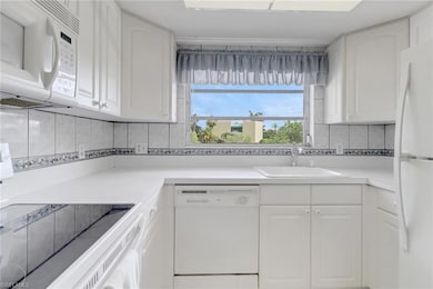Kitchen with white appliances, white cabinetry, decorative backsplash, and light countertops