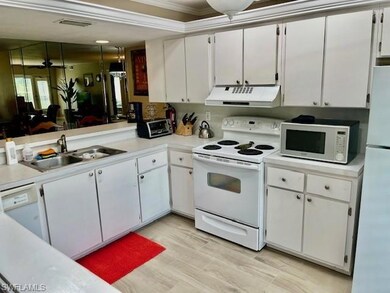 Kitchen with white appliances, white cabinets, light countertops, under cabinet range hood, and light wood finished floors