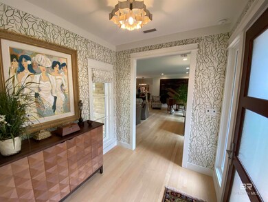 Hallway with visible vents, baseboards, wallpapered walls, light wood-style floors, and a notable chandelier