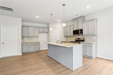 Kitchen with gray cabinetry, stainless steel appliances, tasteful backsplash, light wood-style floors, and baseboards