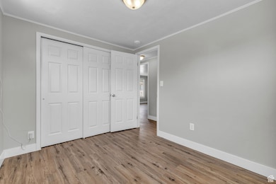 Unfurnished bedroom featuring wood finished floors, ornamental molding, and a closet