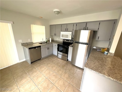 Kitchen featuring stainless steel appliances, gray cabinetry, light tile patterned floors, and light stone countertops