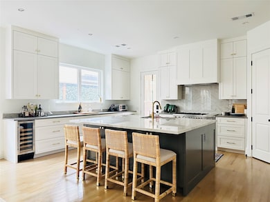 Kitchen featuring light wood-style flooring, a breakfast bar, beverage cooler, light stone countertops, and a kitchen island with sink