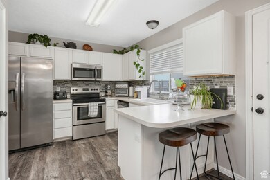 Kitchen featuring sink, white cabinetry, appliances with stainless steel finishes, and a breakfast bar