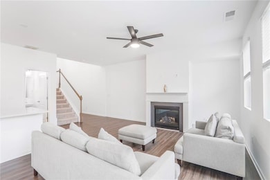 Living room with stairway, ceiling fan, wood finished floors, a glass covered fireplace, and healthy amount of natural light