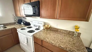 Kitchen featuring black microwave, white electric range, brown cabinets, and light stone countertops