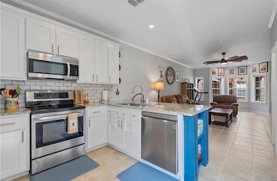 Kitchen featuring appliances with stainless steel finishes, light stone countertops, open floor plan, a peninsula, and crown molding