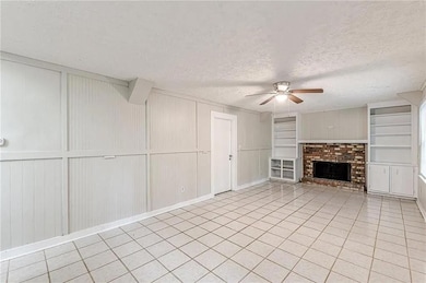 Unfurnished living room with a textured ceiling, light tile patterned floors, a ceiling fan, built in features, and a fireplace