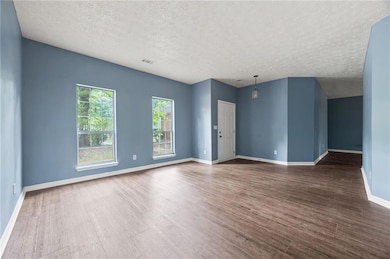 Empty room with a textured ceiling, dark wood-style floors, and baseboards