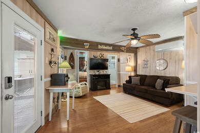 Living room with an AC wall unit, wood walls, a textured ceiling, a ceiling fan, and wood finished floors