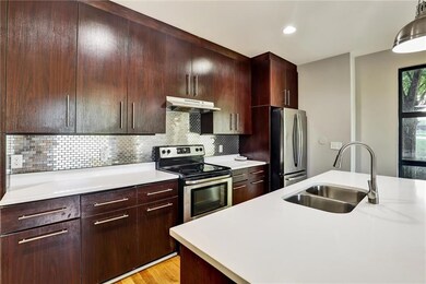 Kitchen with appliances with stainless steel finishes, light countertops, under cabinet range hood, light wood finished floors, and decorative backsplash