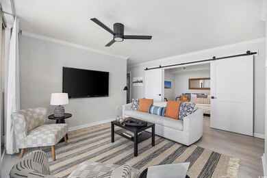 Living room with ceiling fan, light wood-type flooring, a barn door, and ornamental molding