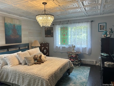 Bedroom with an ornate ceiling, wooden walls, dark wood finished floors, ornamental molding, and a chandelier