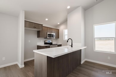 Kitchen featuring stainless steel appliances, a peninsula, light countertops, dark wood-style floors, and vaulted ceiling