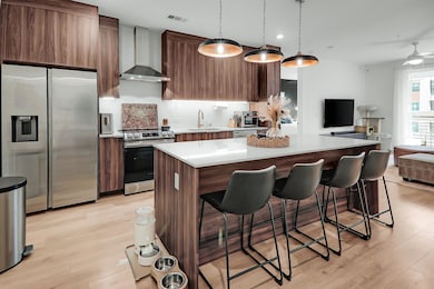 Kitchen featuring appliances with stainless steel finishes, a kitchen island, wall chimney range hood, light countertops, and a breakfast bar
